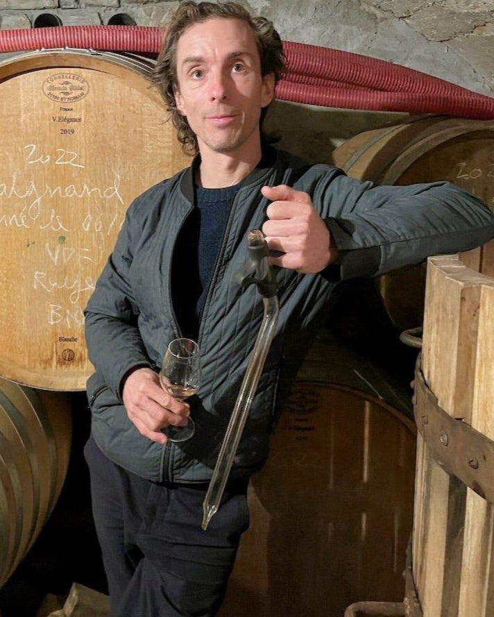 Profile picture of French wine producer Anders Frederik posing in front of some wine barrels while holding a glass. 