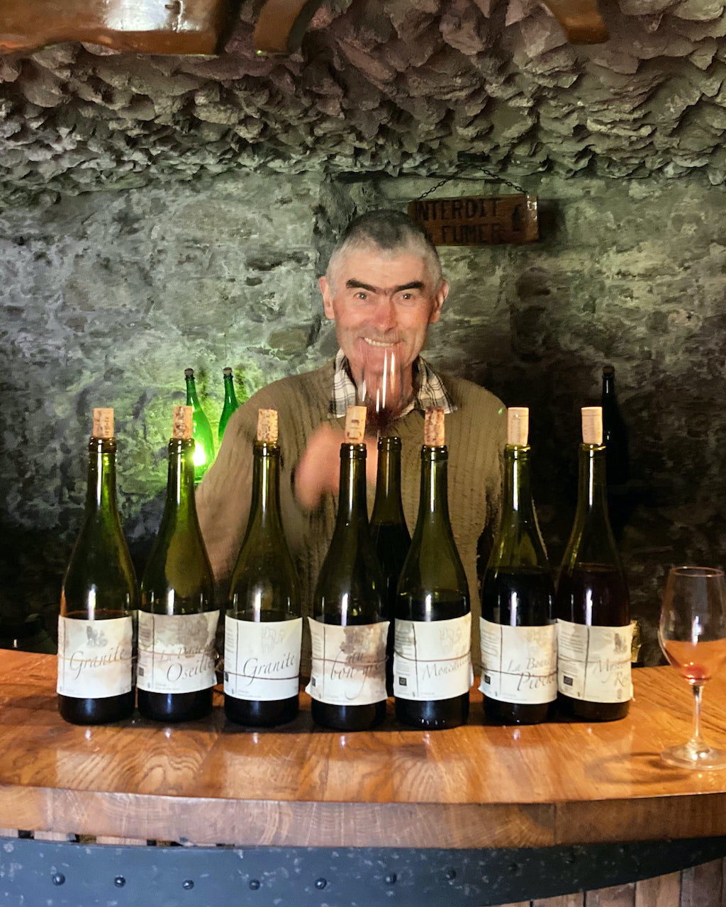 Picture of Michel Guignier standing behind a bar, with seven bottles of his wines standing on the counter.