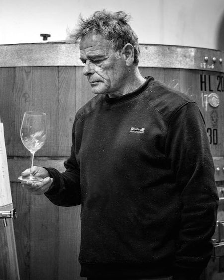 B&W picture of Dario Princic in his cellar, holding a wine glass and apparently swirling the liquid inside.